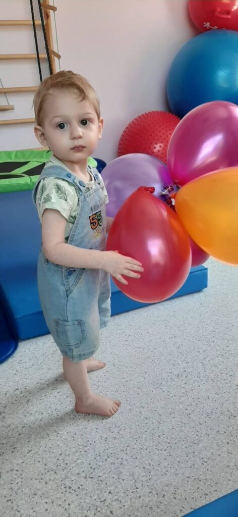 Chłopczyk trzymający kiść napompowanych balonów patrzący głębokim wzrokiem w kierunku osoby robiącej zdjęcie.